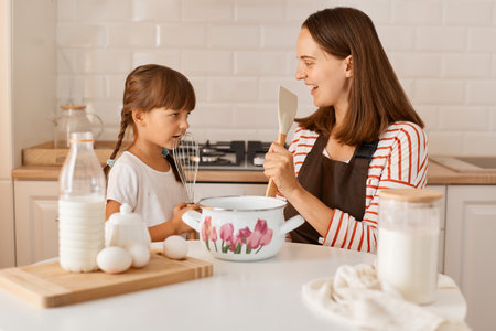Extremely happy excited young adult woman cooking with her daughter at home, having fun together, singing with kitchen equipment, enjoying spending time together.の写真素材