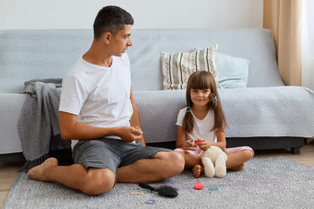 Indoor shot of handsome man listening his daughter attetively, family wearing ccasual style clothing sitting on floor near sofa, spending time for conversation.の写真素材