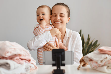 Extremely happy young female blogger broadcasting livestream at home together with her infant...