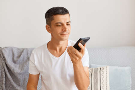 Indoor shot of calm brunette Caucasian handsome man wearing white t shirt posing indoor while...