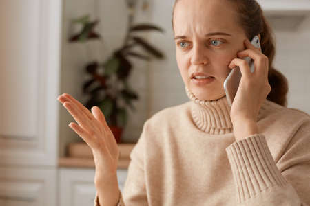 Portrait of confused angry woman wearing beige casual style sweater with ponytail hairstyle having...