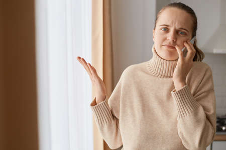 Portrait of puzzled Caucasian young adult woman with ponytail hairstyle wearing beige casual style...