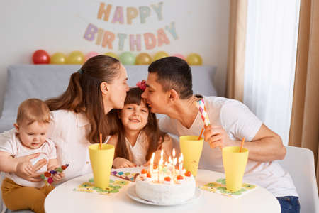 Portrait of charming girl celebrating Birthday with her family, child receiving congratulations at home, parents kissing daughter, congratulating with her day.の写真素材