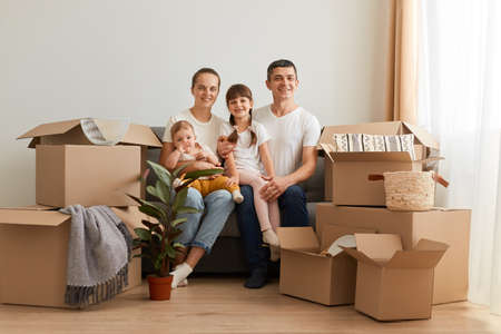 Portrait of smiling couple sitting on sofa with children after moving, looking at camera, expressing happiness after relocating in a new apartment, buying house for their family.の写真素材