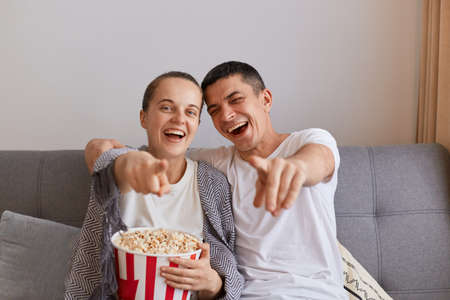 Indoor shot of family, wife and husband, sitting on couch in living room and watching very funny...