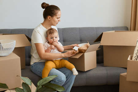 Indoor shot of sad upset woman wearing white t shirt sitting on cough surrounded with cardboard...
