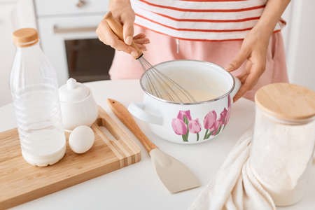 Portrait of anonymous unknown female wearing striped attire dough with whisk in pot, standing near...