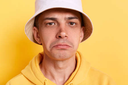 Indoor shot of Caucasian sad upset man wearing casual style hoodie and panama posing isolated over yellow background, standing with pout lips, looking at camera, expressing sorrow.の写真素材