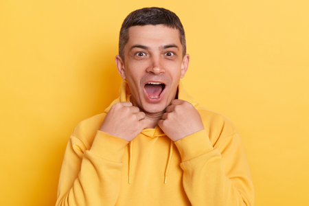 Shocked handsome man wearing casual style hoodie posing isolated over yellow background, looking at...
