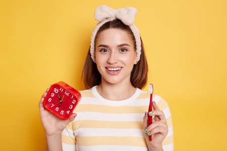 Portrait of happy Caucasian dark haired woman wearing striped shirt and hair band holding alarm...
