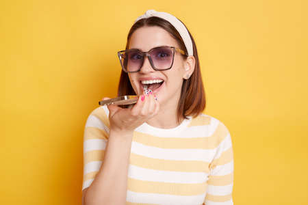 Indoor shot of satisfied happy adorable young woman wearing striped t-shirt posing isolated over...