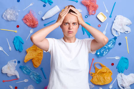 Portrait of desperate young adult picked plastic litter isolated on blue wall, standing with hands...