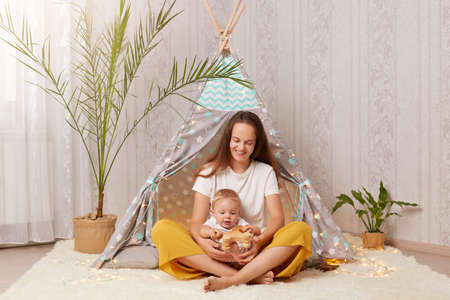 Smiling satisfied woman with long dark hair wearing white t shirt sitting in peetee tent with her...