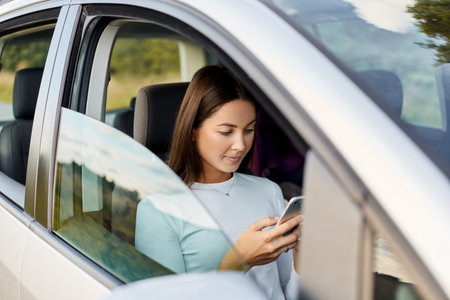 Side view of attractive adorable woman with dark hair wearing white shirt sitting in her car using...