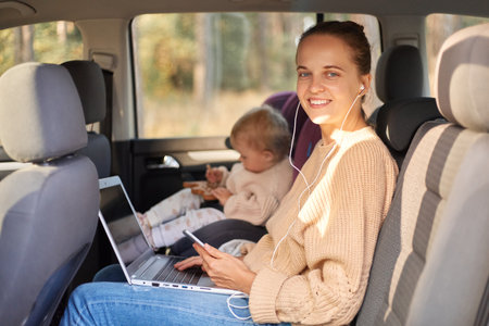 Portrait of smiling woman sitting with her baby daughter in safety chair on backseat of the car,...