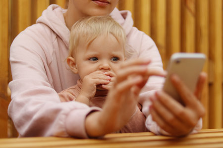 Portrait of faceless woman sitting and using cell phone, holding baby daughter in hands, unknown female typing on mobile phone, checking social networks.の写真素材