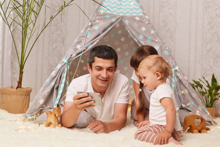 Portrait of satisfied delighted Caucasian man wearing white t-shirt with his children posing on...