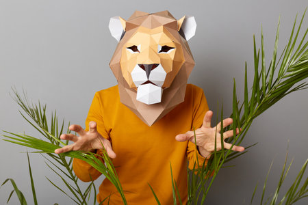 Portrait of scary anonymous man wearing lion mask and orange sweatshirt isolated over gray background, showing his paws, trying to frighten, posing with raised arms.の写真素材