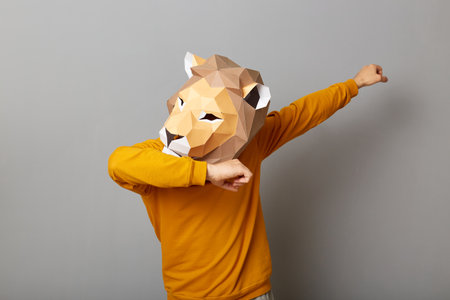 Indoor shot of anonymous man wearing lion mask and orange sweatshirt isolated over gray background, making dabbing movement, famous internet meme of success victory.の写真素材