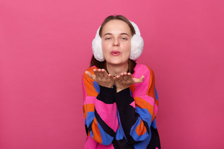 Image of romantic flirting lovely woman wearing winter earmuffs and warm sweater posing isolated...