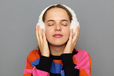 Indoor shot of calm beautiful adorable woman wearing colorful sweater posing isolated over gray...