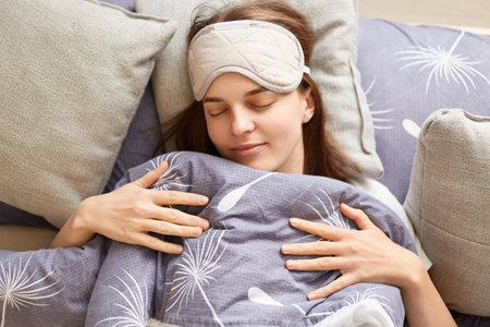 Top view portrait of dark haired Caucasian sleepy positive attractive woman lying in bed under gray...