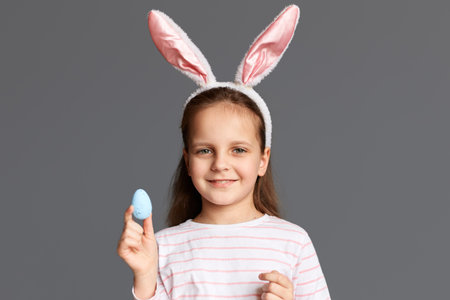 Photo of charming cute positive little child girl wearing bunny ears holding Easter eggs painted by...