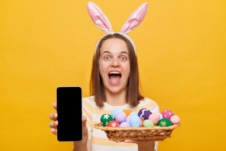 Portrait of happy joyful young adult woman wearing rabbit ears holding colorful Easter in wicker...