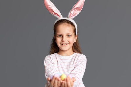 Photo of satisfied little girl wearing bunny ears holding Easter eggs, found many testicles during...