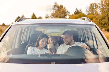 Man and woman driving in the car with their little daughter, stop for break, wife showing phone to husband, family expressing positive emotions. Leisure, travel, tourism.の写真素材