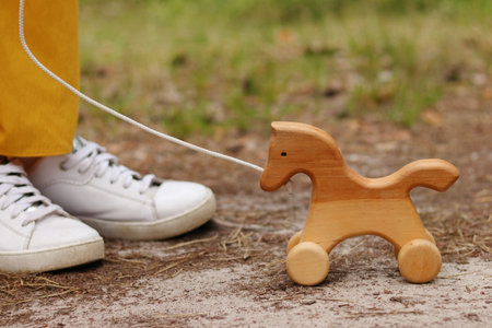 Image of faceless person, legs of woman standing near wooden eco horse in the playground on the grass, eco toys for children.の写真素材