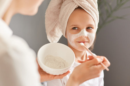 Unrecognizable mother and little daughter posing at home together smiling happy child with cream on face looking smiling at mommy family beauty treatment.の写真素材