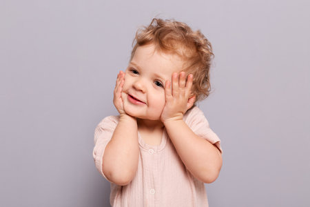 Cute charming smiling infant baby little caucasian girl posing isolated over gray background looking...