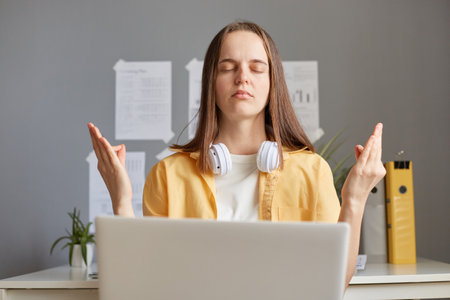 Calm relaxed woman freelance working on her laptop, enjoying peace and quiet of her home office, meditating and relaxing while having a break, online remote job.の写真素材