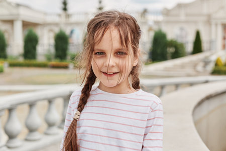 Smiling little girl wearing striped shirt posing in town with beautiful historical architecture enjoying sightseeing in summer looking at camera with happy face.の写真素材