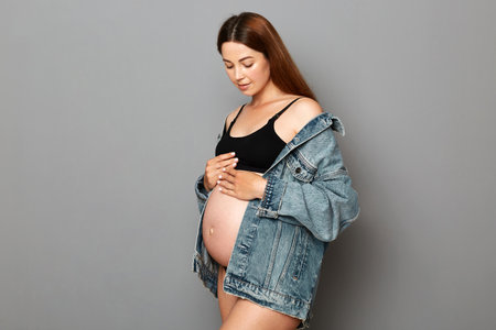 Beautiful dark haired pregnant woman caressing her belly isolated on gray background future mother...