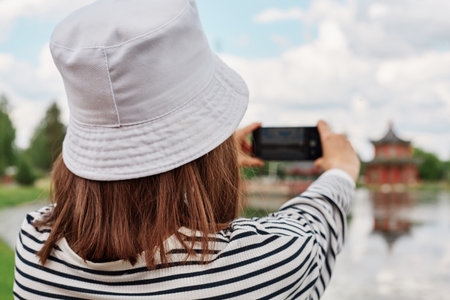 Woman in summer lake, river pond, photographing landscape on smartphone, view from back, recording a...