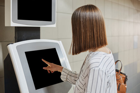 Unrecognizable brown haired woman using the self services terminal to pay on the fare or paying for credit online.の写真素材