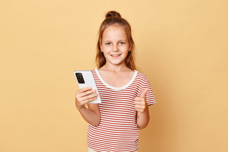 Cute optimistic smiling little brown haired girl wearing striped t-shirt standing isolated over...