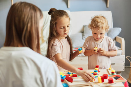 parent-child bonding. Happy family time. Playful daycare activities. parenting joy moments. Children playing together with mother with wooden sorter toys at home interiorの写真素材