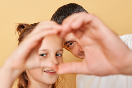 Smiling brwon haired little girl standing with her father and making heart shape with hands together in fron of their faces expressing love family realtionship.の写真素材