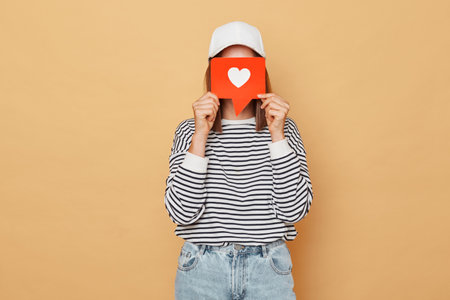 Unrecognizable woman wearing striped shirt and baseball cap hiding her face behind like blogger icon...