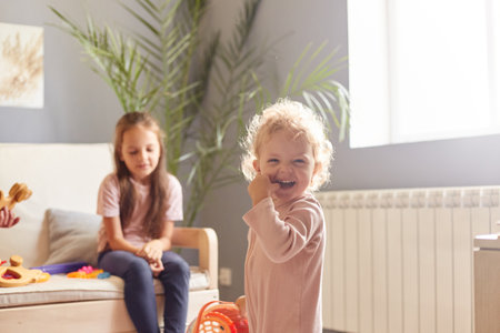 Two cute little girls sisters playing with toys in living room together, preschool kids enjoying playtime, having fun at home expressing happiness.の写真素材