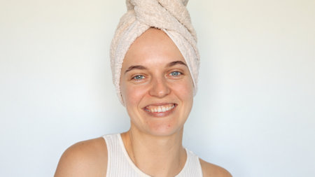 Cute charming beautiful young woman with bath towel on head looking at camera with toothy smile enjoying beauty morning routine isolated over white backgroundの写真素材