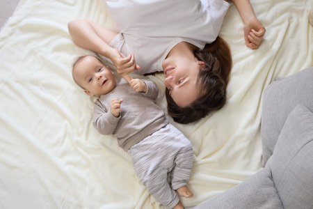 Top view of Caucasian mom lying with her small infant daughter or son in bedroom creating playful environment filled with happiness and innocence bonding familyの写真素材