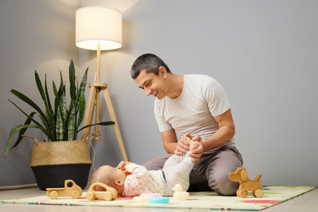 Brunette Caucasian man playing with newborn daughter or son indoors loving father spending time...