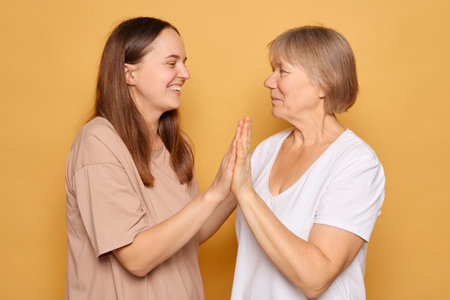 In a warm, vibrant yellow setting, a young woman and an older woman engage in a lively exchange, expressing joy and warmth while maintaining eye contact and smiling at each other.の写真素材
