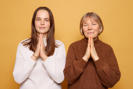 The two women present a calm and respectful gesture with their hands held in prayer. They are framed by a vibrant yellow backdrop, creating a warm and inviting atmosphere.の写真素材