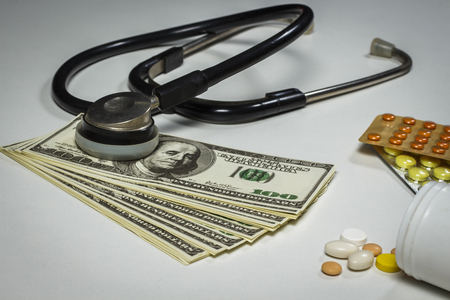 Pills, a stethoscope and money on a white tableの写真素材