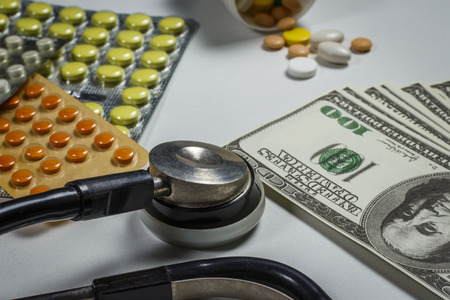 A lot of pills, a stethoscope and money on a white tableの写真素材